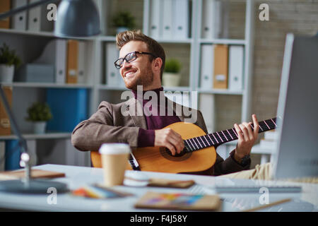 Handsome businessman playing the guitar by desk in office Stock Photo