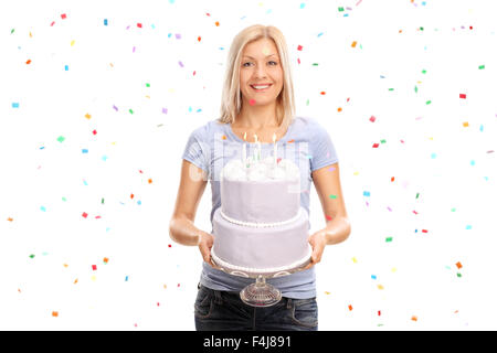 Joyful young woman holding a birthday cake and smiling with confetti streamers in the air all around her Stock Photo