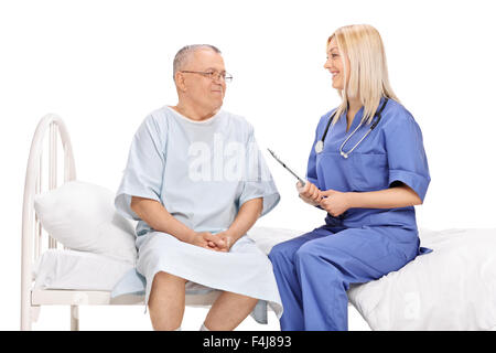Mature male patient and a young female doctor having a conversation seated on a hospital bed isolated on white background Stock Photo
