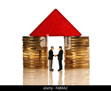 Two businessmen shaking hands under a red roof, which rests on coins. Stock Photo