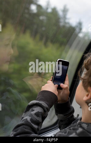 Orebro, Boy looking through window and taking picture by mobile phone Stock Photo