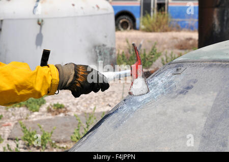 Firefighter uses an axe to break the front windshield of a car to rescue the trapped driver and passengers Stock Photo