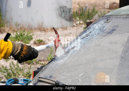 Firefighter uses an axe to break the front windshield of a car to rescue the trapped driver and passengers Stock Photo