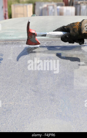 Firefighter uses an axe to break the front windshield of a car to rescue the trapped driver and passengers Stock Photo