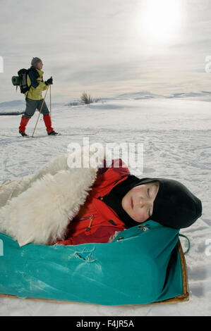 Boy sleeping on sleeping bag with woman walking in the background Stock Photo