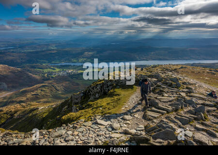 Hikers walking up the last ridge onto the summit of the Old Man of Coniston with views over Coniston Water, Lake District Stock Photo