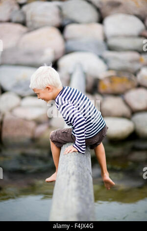 Boy sitting on log over stream Stock Photo