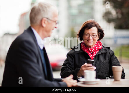 Mature couple sitting at cafe, woman text messaging on phone Stock Photo