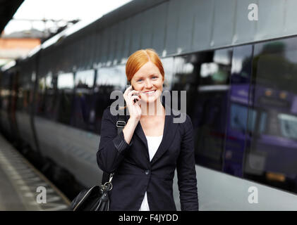 Portrait of young smiling woman talking via mobile at train station Stock Photo