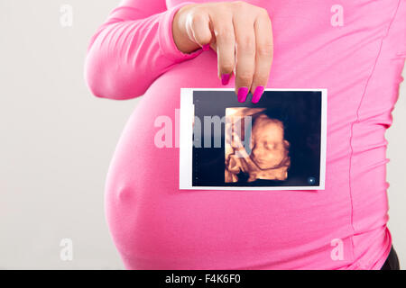 Pregnant woman holds ultrasound photo on the belly Stock Photo