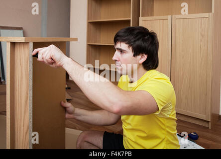 Young man sitting on floor assembling flatpack closet Stock Photo