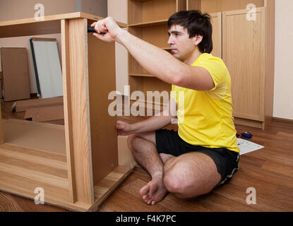 Young man sitting on floor assembling flatpack closet Stock Photo