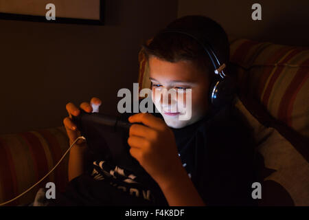 Single Teenage Caucasian Boy looking at tablet computer while listening through headphones Stock Photo