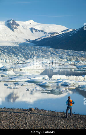 Person beside Fjallsarlon iceberg lagoon, beneath Fjallsjokull glacier. Vatnajokull National Park, Sudhurland, Iceland. Stock Photo