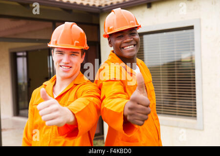 cheerful young construction workers thumbs up outside the house Stock Photo