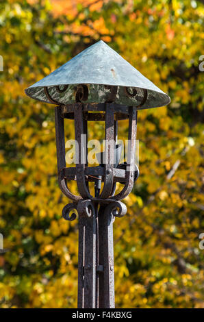Closeup of an antique wrought iron outdoor lamp with fall colors in the background Stock Photo