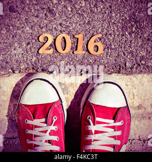 high-angle shot of some wooden numbers forming the number 2016, as the new year, and the feet of a man wearing red sneakers on t Stock Photo