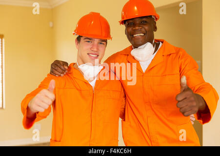 cheerful workmen giving thumbs up inside house Stock Photo
