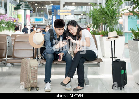 Young Asian couple using smart phone while sitting in the airport terminal waiting for boarding. Stock Photo