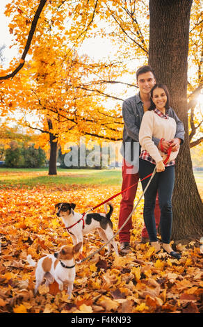 Portrait of young couple with two little dogs on walk in park on autumn day Stock Photo