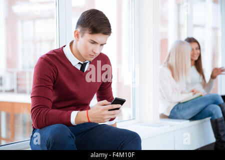 Portrait of a young man using smartphone in university hall Stock Photo