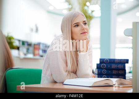 Portrait of a thoughtful blonde woman sitting at the table with books in university library Stock Photo