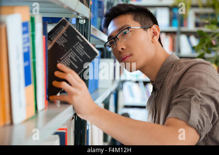 Portrait of a young asian man searching book in library Stock Photo
