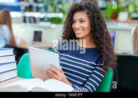 Portrait of a happy afro american female student sitting at the table with tablet computer in classroom and looking away Stock Photo