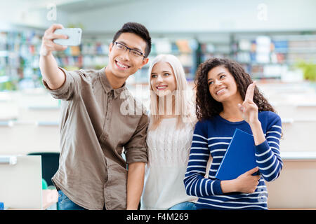Asian boy in black glasses, blonde beautiful girl and african american curly woman are making selfie using cellphone Stock Photo