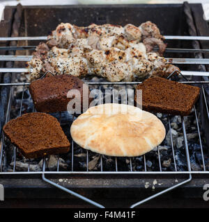 Flat cake, slices of brown bread and shish kebab from meat warmed on a brazier Stock Photo