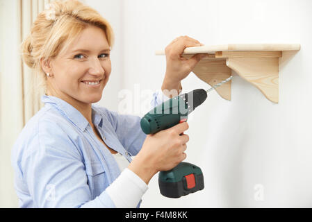 Woman Putting Up Wooden Shelf At Home Using Cordless Drill Stock Photo