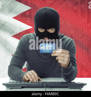 Dark-skinned hacker with credit card in hand and flag on background - Bahrain Stock Photo