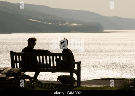 A young couple talk on a bench while overlooking the British coastline, Britain, UK Stock Photo
