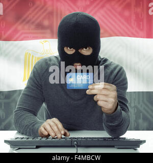 Dark-skinned hacker with credit card in hand and flag on background - Egypt Stock Photo