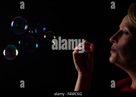 Woman blowing soap bubbles on black background Stock Photo
