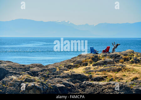 People sitting reading in lounge chairs overlooking Oak Bay, Victoria, British Columbia, Canada Stock Photo