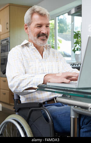 Disabled Man In Wheelchair Using Laptop At Home Stock Photo