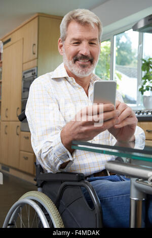 Disabled Man In Wheelchair Texting On Mobile Phone At Home Stock Photo