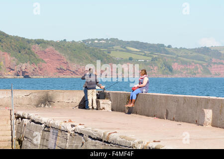 Men fishing with woman sat on the sea wall at Babbacombe Beach on hot summers day in Torquay, Devon, England Stock Photo