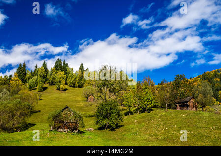 Fall colors around a cottage house. Autumn landscape in mountains with colorful forest and blue sky. Stock Photo