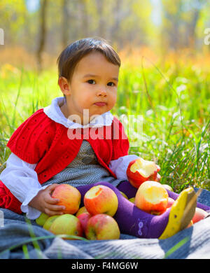 child with red apples sitting on leaves in autumn park Stock Photo