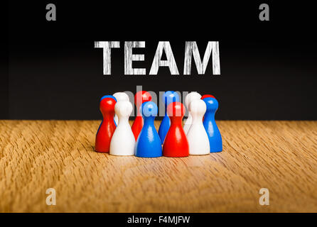 Concept for team, teamwork with white chalk text. Red white blue pawn figures and black background on oak. Stock Photo