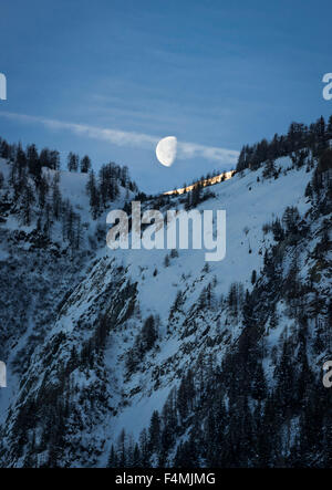The moon is setting on a snow covered mountain peak in the Swiss alps, seen from Blatten, Switzerland (canton Valais) Stock Photo