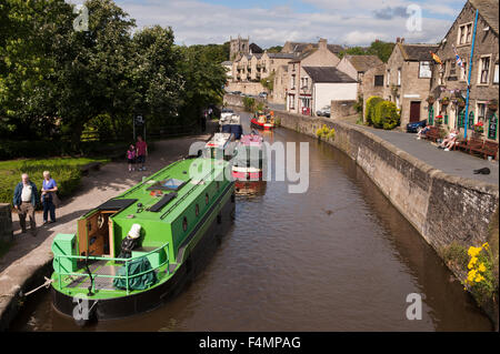 Sunny summer high view of canal boats moored, people & dog relaxing on towpath - Springs Branch, Leeds-Liverpool Canal, Skipton, Yorkshire, England. Stock Photo