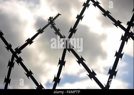 Razor wire fencing silhouetted against a cloudy blue sky in the UK. Stock Photo