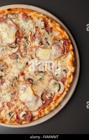 Pizza on a wooden plate with mushrooms, smoked ham and mozzarella Stock Photo