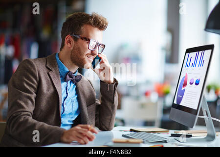 Busy employee speaking on the phone while looking at computer screen Stock Photo