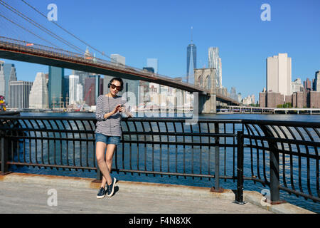 USA, New York City, portrait of  young woman hearing music with headphones in front of skyline Stock Photo