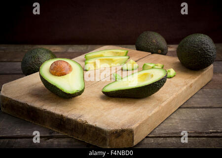 Whole and sliced avocado on wooden board Stock Photo