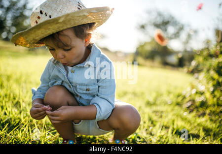 Little girl wearing straw hat crouching on a meadow Stock Photo